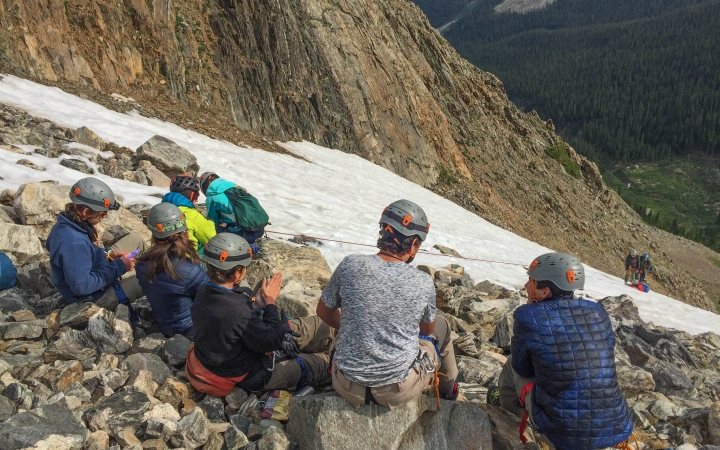 a group of students with helmets on rest on rocks on a mountaineering course with outward bound